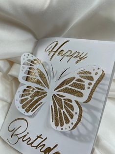 a white and gold birthday card with a butterfly on it's back that says, happy birthday