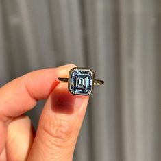 a person holding a ring with an aqua blue diamond in it's middle finger