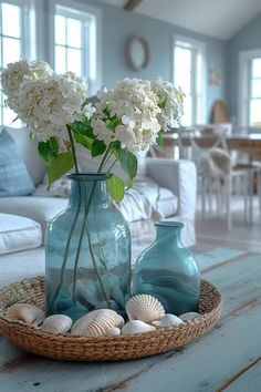 two vases filled with white flowers on top of a table next to sea shells