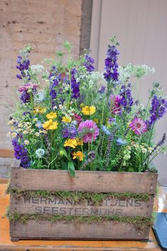 a wooden box filled with lots of different types of wildflowers and grass on top of a table