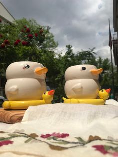 two plastic ducks sitting on top of a table next to each other in front of trees