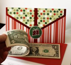 a hand is holding a roll of money in front of an envelope with a gift on it