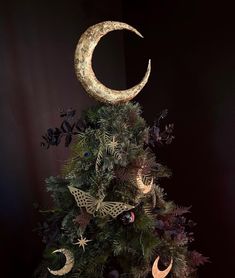 a christmas tree decorated with gold moon and stars on it's top, in front of a black background