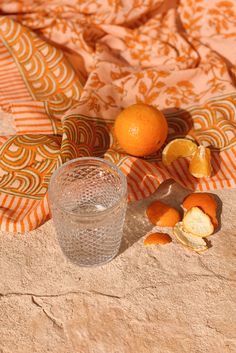 an orange sitting on top of a blanket next to a glass filled with water and fruit