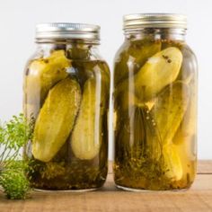 two jars filled with pickles sitting on top of a wooden table