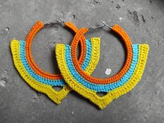 two pairs of crocheted hoop earrings on top of a cement floor, one with yellow and blue beads