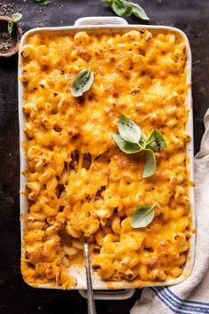 a casserole dish with macaroni and cheese topped with fresh sage leaves