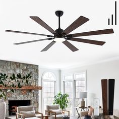 a ceiling fan in a living room with stone fireplace and large window behind the couch