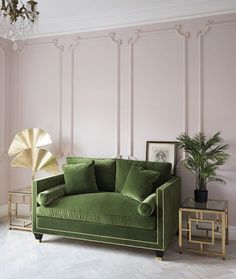 a living room with pink walls and green velvet couch in the center, gold side tables on either side