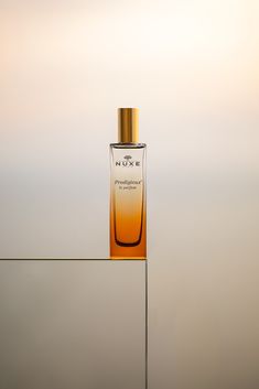 a bottle of perfume sitting on top of a glass shelf in front of a wall