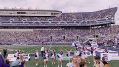 a group of people standing on top of a field holding up purple and white signs