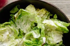 a bowl filled with lettuce sitting on top of a wooden table next to an apple