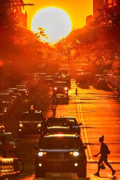 the sun is setting over a busy street with cars and people walking on the sidewalk