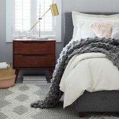 a bedroom with gray walls, white bedding and a grey blanket on the headboard