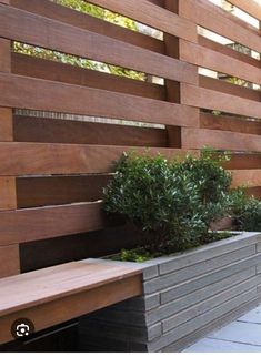 a wooden bench sitting in front of a wall next to a planter filled with plants