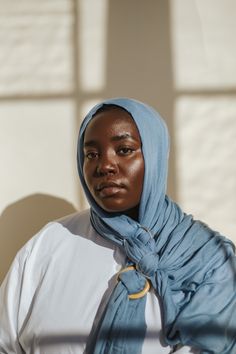 a woman wearing a blue scarf standing in front of a window with sunlight streaming through it