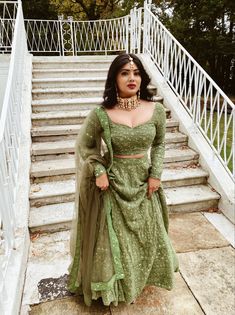 a woman in a green lehenga standing on steps with her hands behind her back