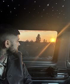 a man sitting in the passenger seat of a car looking out the window at the sunset