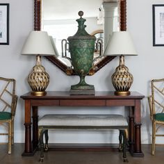 a table with two lamps on it and a mirror in the corner behind it,