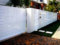 a white fence in front of a brick sidewalk and palm trees on the other side