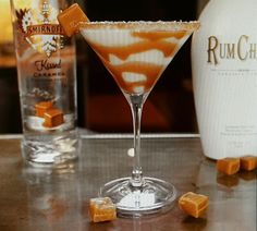 a drink in a martini glass with caramel on the rim next to some liquor bottles