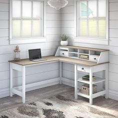 a computer desk with a laptop on it in front of two windows and a rug