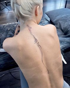 the back of a woman's neck with a feather tattoo on her left shoulder