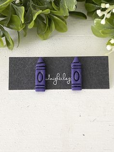 two purple plastic objects sitting on top of a black piece of paper next to green leaves