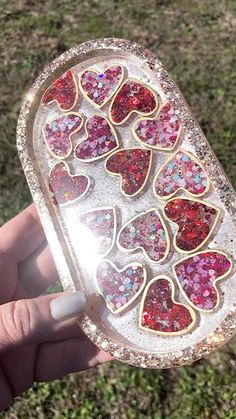 someone holding up a heart shaped box with glitter hearts on it's sides in the grass