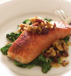 a white plate topped with salmon and greens on top of a bed of beans, broccoli