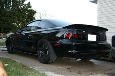 a black sports car parked in front of a house with its hood up and tail lights on