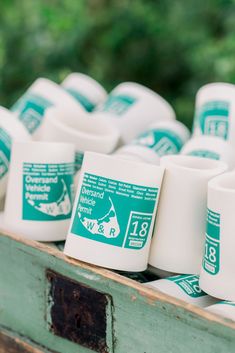 several white cups are stacked on top of each other in a wooden box with trees in the background