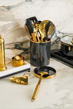 gold kitchen utensils in a black and white container on a marble countertop