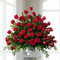 a vase filled with lots of red roses on top of a table next to a window