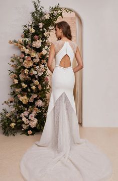 a woman standing in front of flowers wearing a white gown with open back and sheer lace detailing