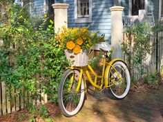 a yellow bicycle with flowers in the basket is parked next to a fence and house