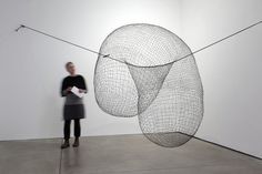 a woman standing in front of a sculpture with wires hanging from it's sides