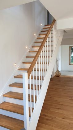 a white staircase with wooden handrails and lights on the bottom part of it