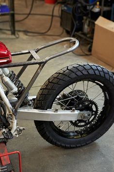 a red motorcycle parked in a garage next to a box and some other items on the floor