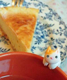 a piece of cheese cake on a plate with a small cat figurine