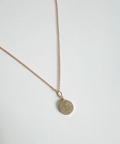 a gold necklace with a coin hanging from it's side on a white surface