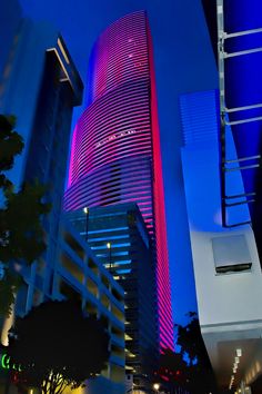 two tall buildings with neon lights in the city at night, one building has a red and blue light on it's side