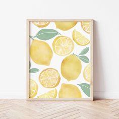 a yellow lemon print with green leaves on a white wall next to a wooden floor