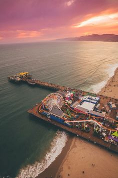 an amusement park next to the ocean at sunset or sunrise with colorful clouds and water