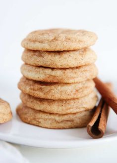 a stack of cinnamon sugar cookies on a white plate with cinnamon sticks next to it