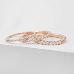 three rose gold wedding rings with diamonds on top of a white surface, one in the middle