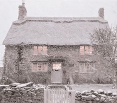 a stone house covered in snow next to a fence and gate with lights shining through the windows