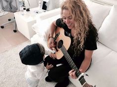 a woman sitting on top of a white couch next to a child holding an acoustic guitar