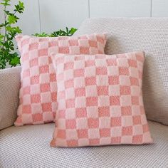 two pink pillows sitting on top of a couch next to a potted green plant