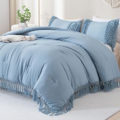 a blue comforter with fringe trim and pillows on a white carpeted room floor